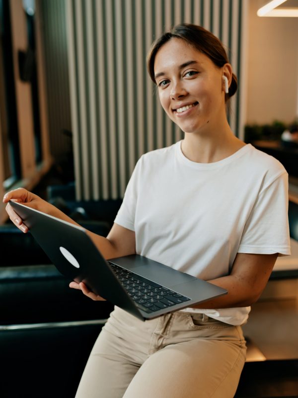 charming-pretty-lady-with-wonderful-smile-and-dark-collected-hair-dressed-white-tshirt-and-beige-pants-is-working-at-office-with-laptop